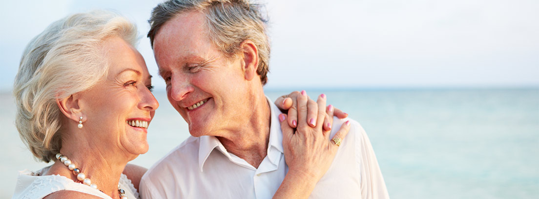 Hombre y mujer mayores en la playa abrazándose y sonriéndose