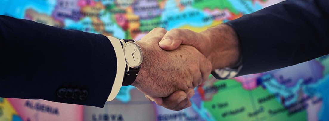 Manos estrechándose delante de un mapa del mundo como metáfora de los acuerdos bilaterales entre dos países