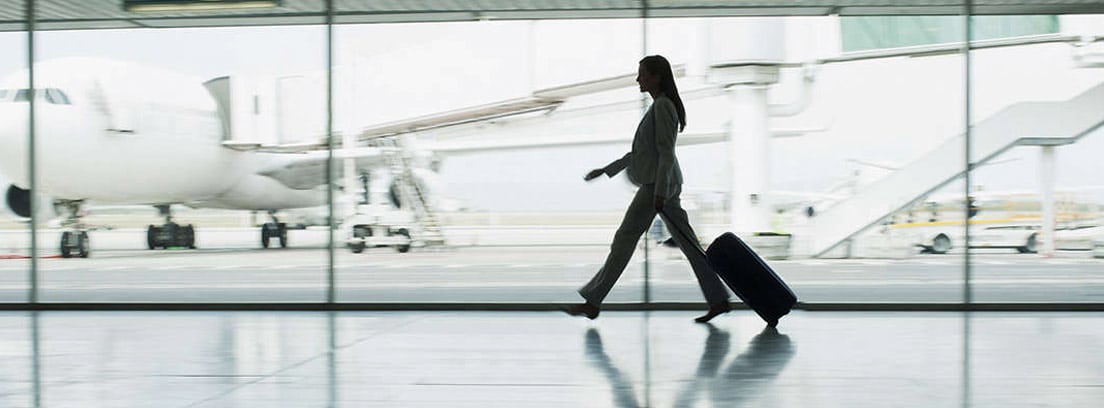 Mujer emprendedora con una maleta por un pasillo de un aeropuerto