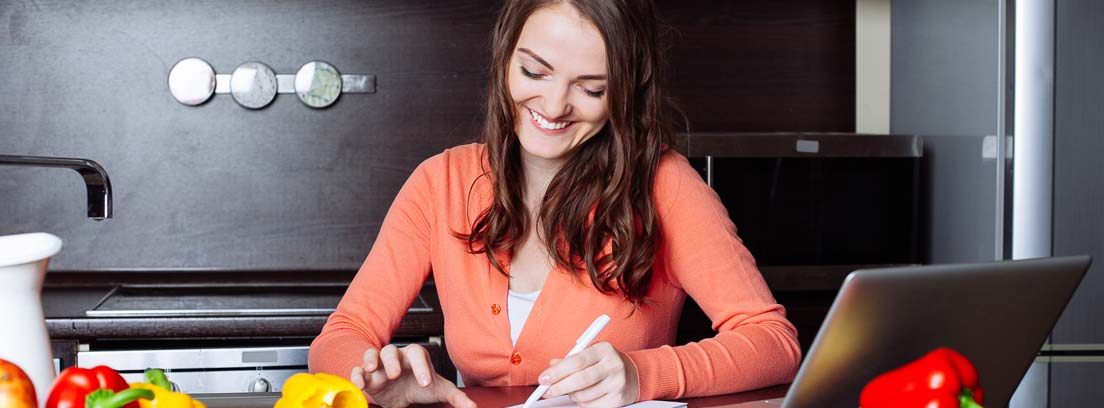 Mujer sonriente revisando contabilidad doméstica en la cocina