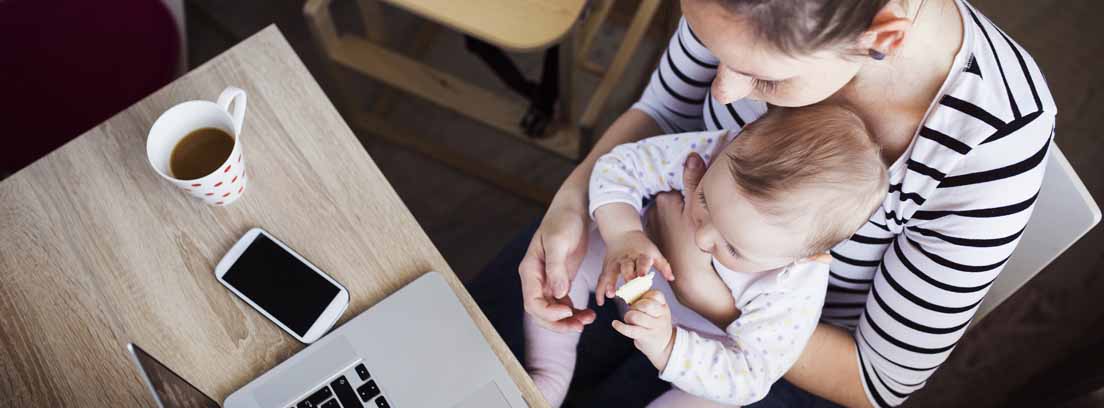 Mujer con bebé y apuntando en un cuaderno delante de ordenador