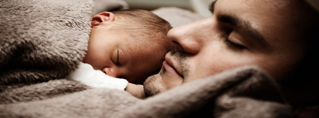 Un hombre y un bebé tapados con una manta durmiendo
