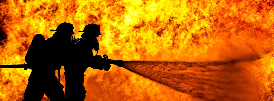 Silueta de dos bomberos delante de un fuego con una manguera, antes de llegar a la edad de jubilación de los bomberos