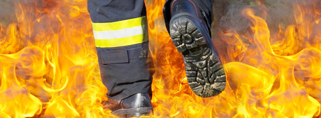 Piernas con uniforme de bombero pisando sobre unas llamas