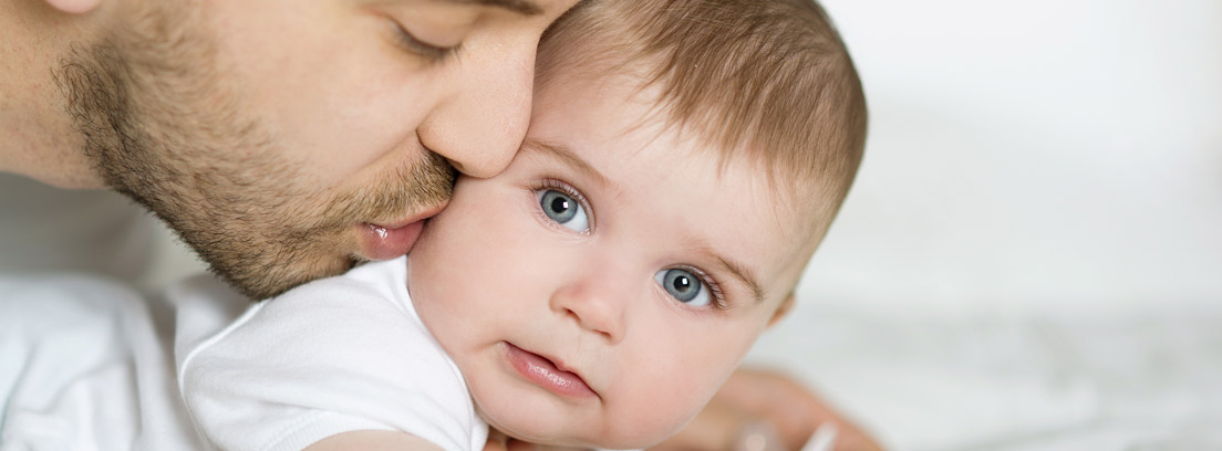 Hombre dando un beso a un bebé durante una excedencia por cuidado de hijos