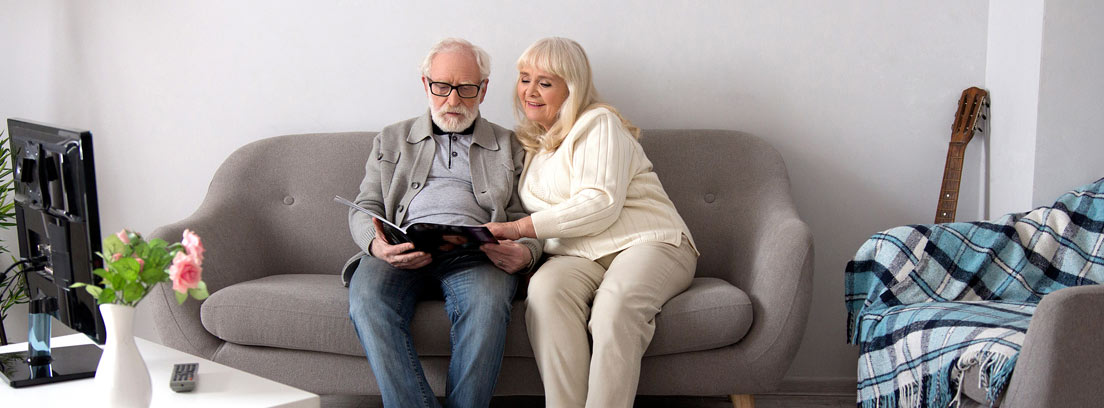 Pareja de ancianos sentados en un sofá leyendo un libro tras vender su casa en nuda propiedad