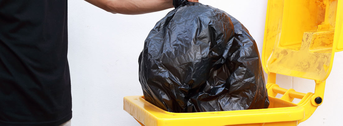Hombre tirando una bolsa de basura a un contenedor amarillo