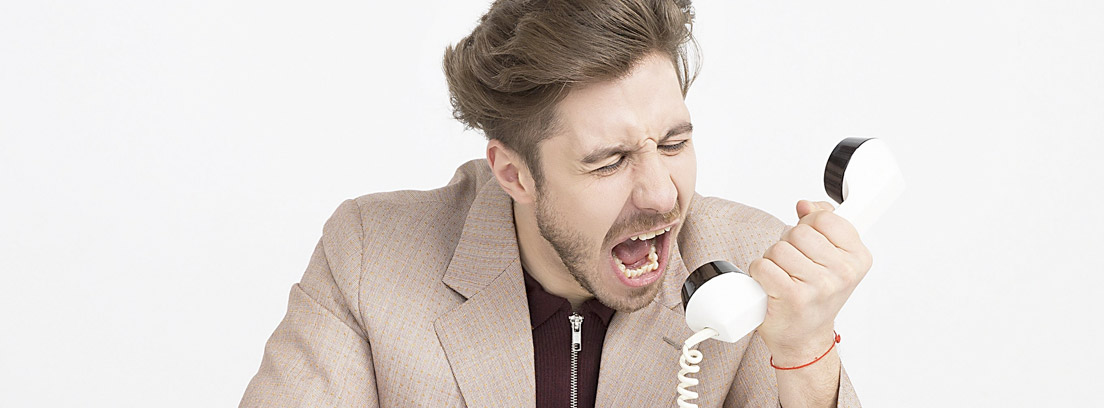 Hombre grita hacia auricular de teléfono fijo clásico de color blanco
