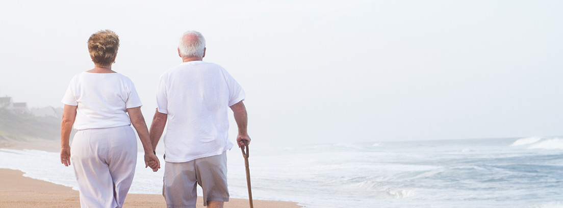 Dos personas mayores de espaldas caminando por la playa cogidos de la mano