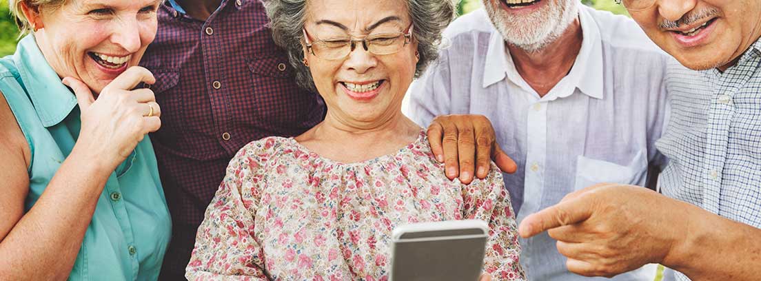 Grupo de personas mayores sonrientes mirando un teléfono móvil
