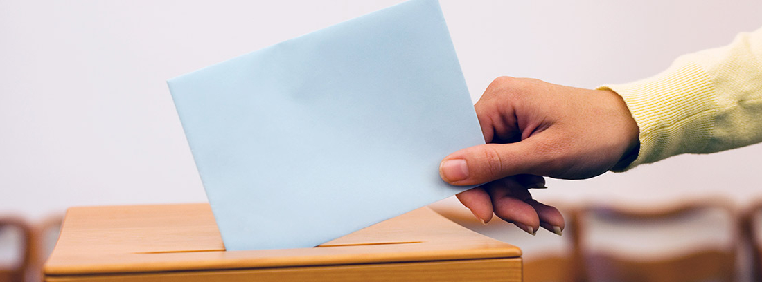 Mano de mujer metiendo un sobre con su voto en una urna