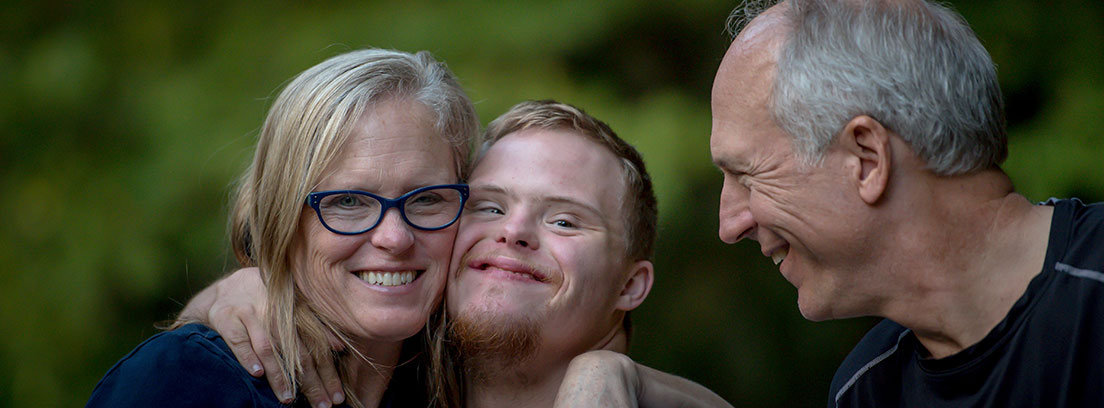 Mujer abraza a chico con síndrome de Down y otro hombre les mira