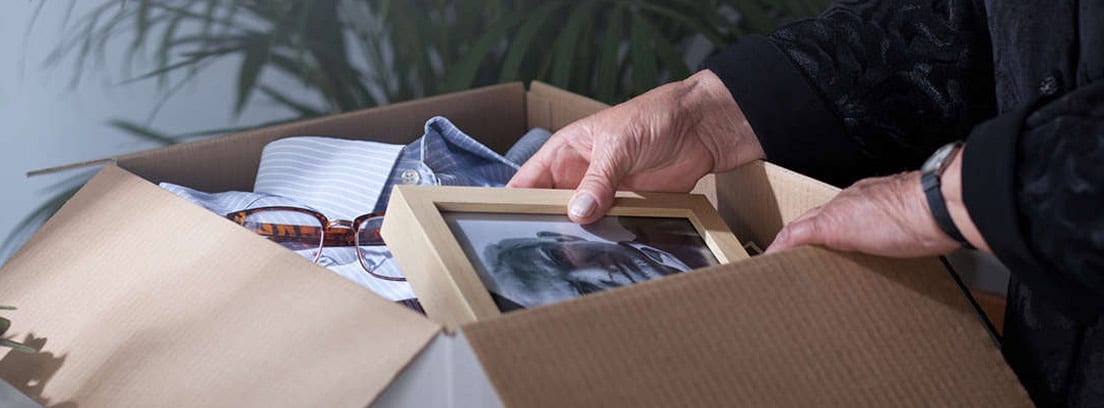 Manos de una anciana guardando una fotografía en una caja de cartón