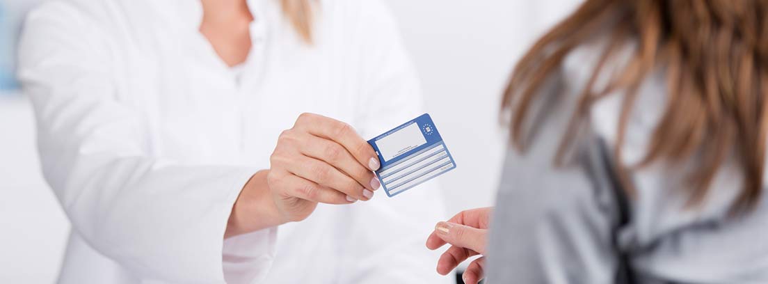 Mujer con bata blanca entregando una tarjeta sanitaria a otra mujer