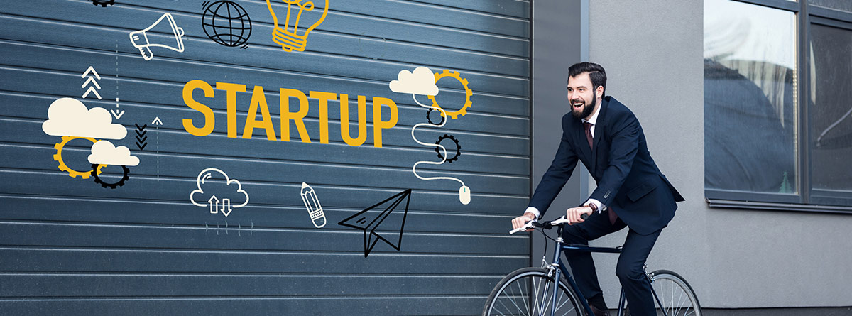 chico pasando en bicicleta por delante de una puerta con el cartel de Startup