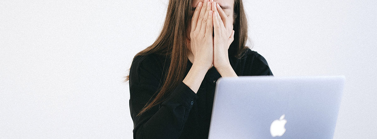 Mujer tapándose la cara frente a un ordenador.